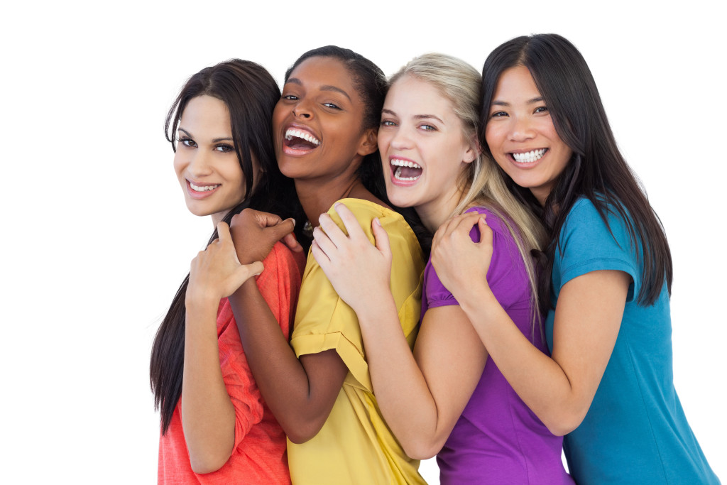 Diverse young women laughing at camera and embracing on white background