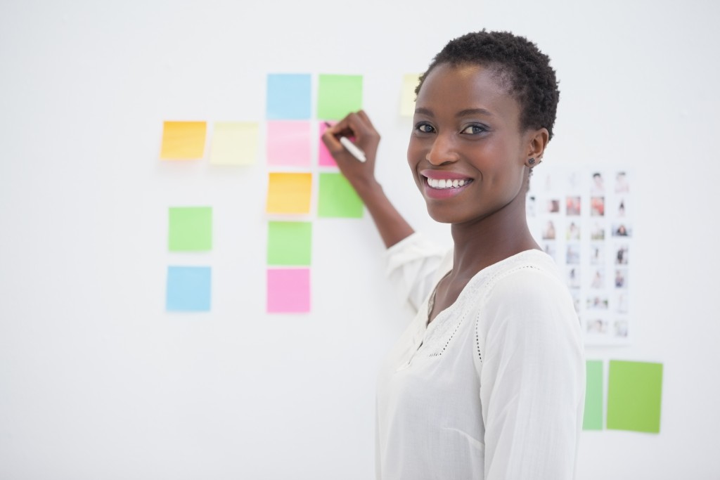 Smiling designer writing on sticky notes and looking at camera