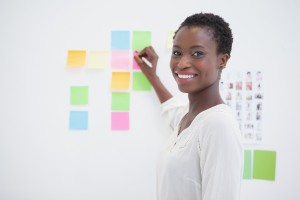 Smiling designer writing on sticky notes and looking at camera - image creativity_mainimage-300x200 on https://thedreamcatch.com