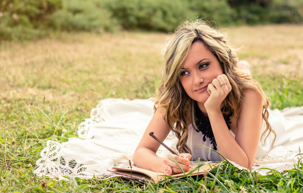 Romantic girl writing in a diary lying down outdoors