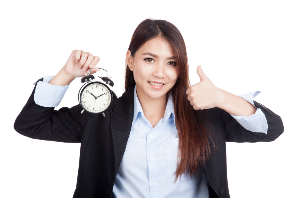 Young Asian businesswoman thumbs up with alarm clock