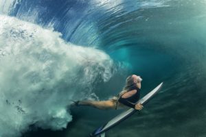 A blonde surfer girl underwater doing duck dive holding surfing - image flow-surfer-300x200 on https://thedreamcatch.com